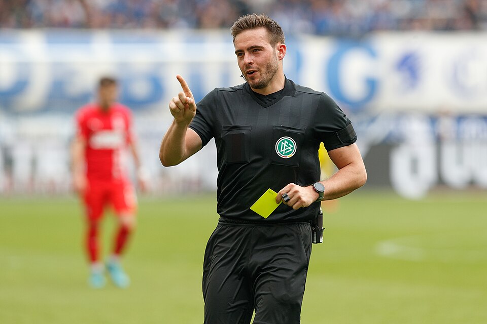 Árbitro mostrando tarjeta amarilla a un jugador en un partido tenso